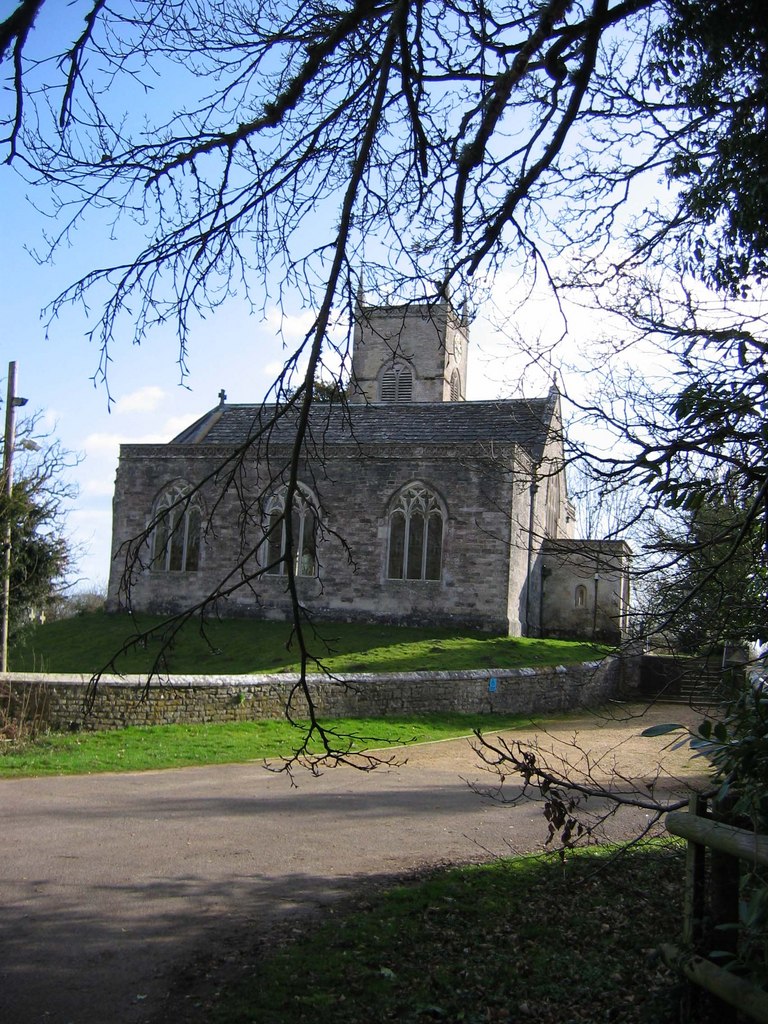 St Nicholas Church on a sunny day, with three Gothic windows, blue sky and green grass framed by tree branches